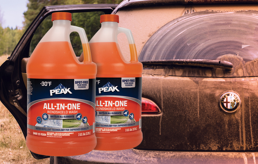 PEAK All-In-One Windshield Wash orange bottles in front of dirty back windshield.